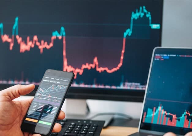 A person monitoring stock market trends and technical indicators on a smartphone and computer.